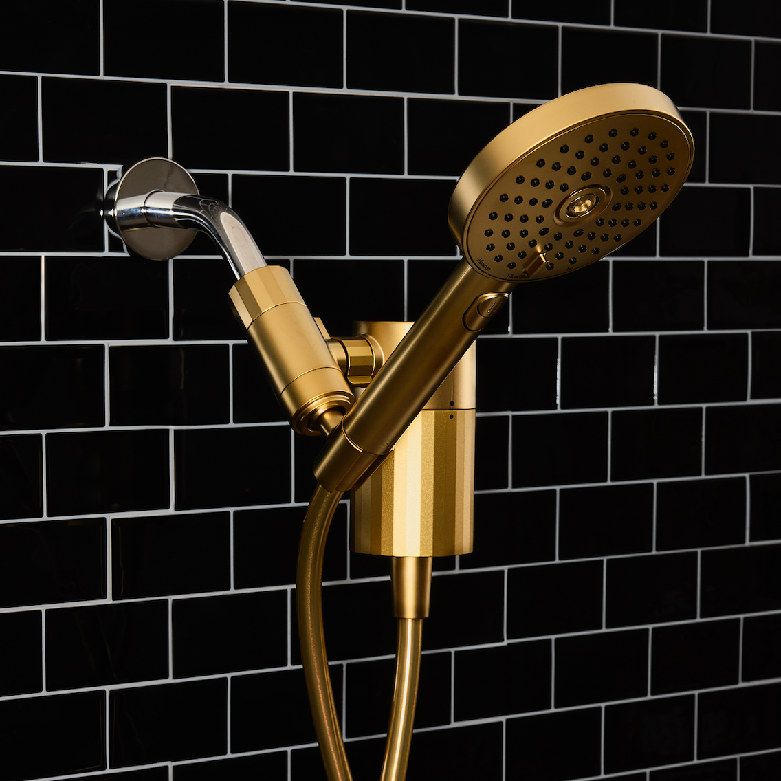 Gold filtered shower head and handheld shower against a black tiled wall