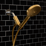 Gold shower head and handle against a black tiled wall