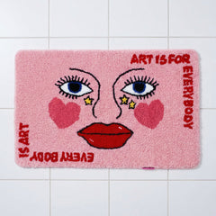 Plush pink bathroom mat with abstract face graphic and text.