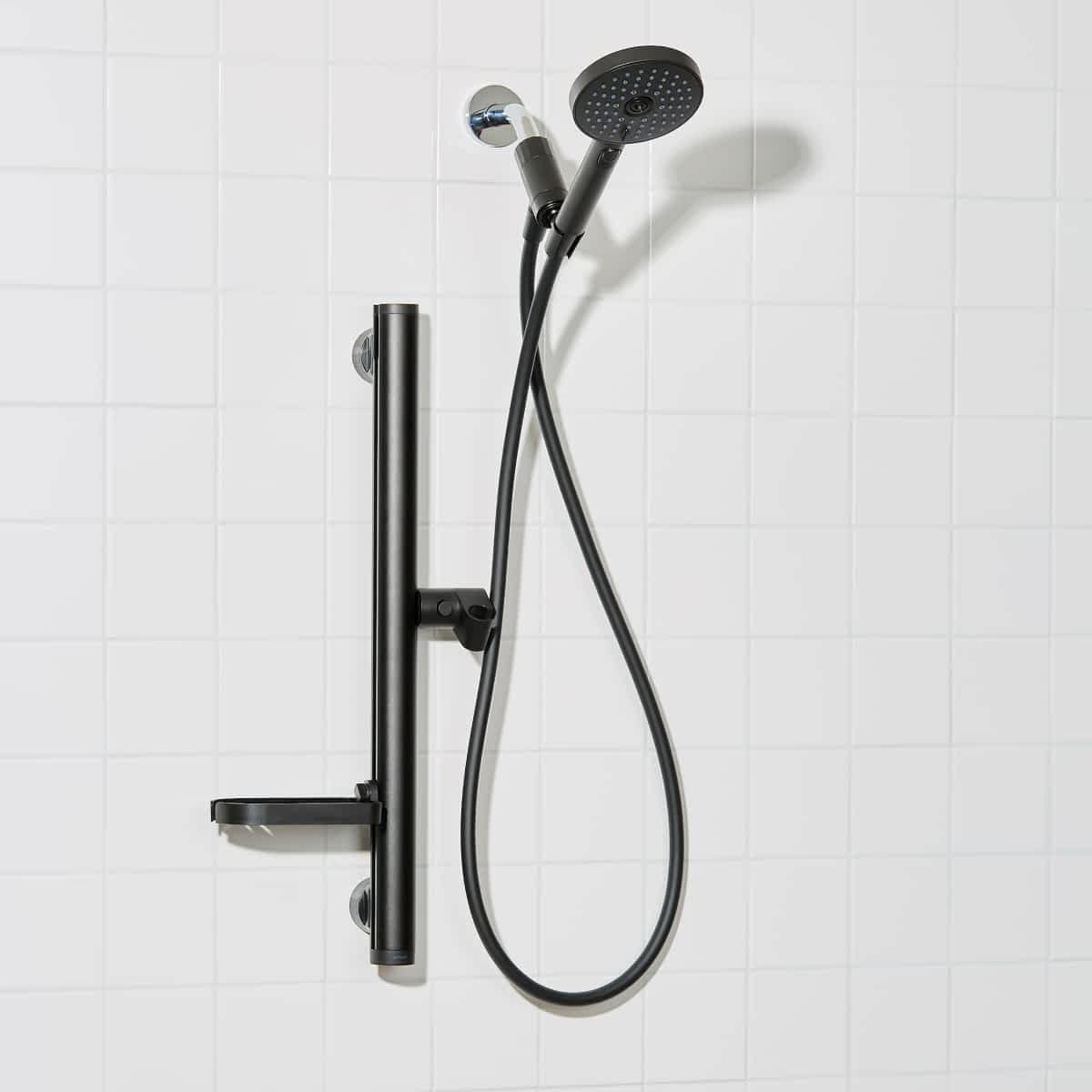 Black shower kit with handheld shower head and control handle on a white tiled wall background