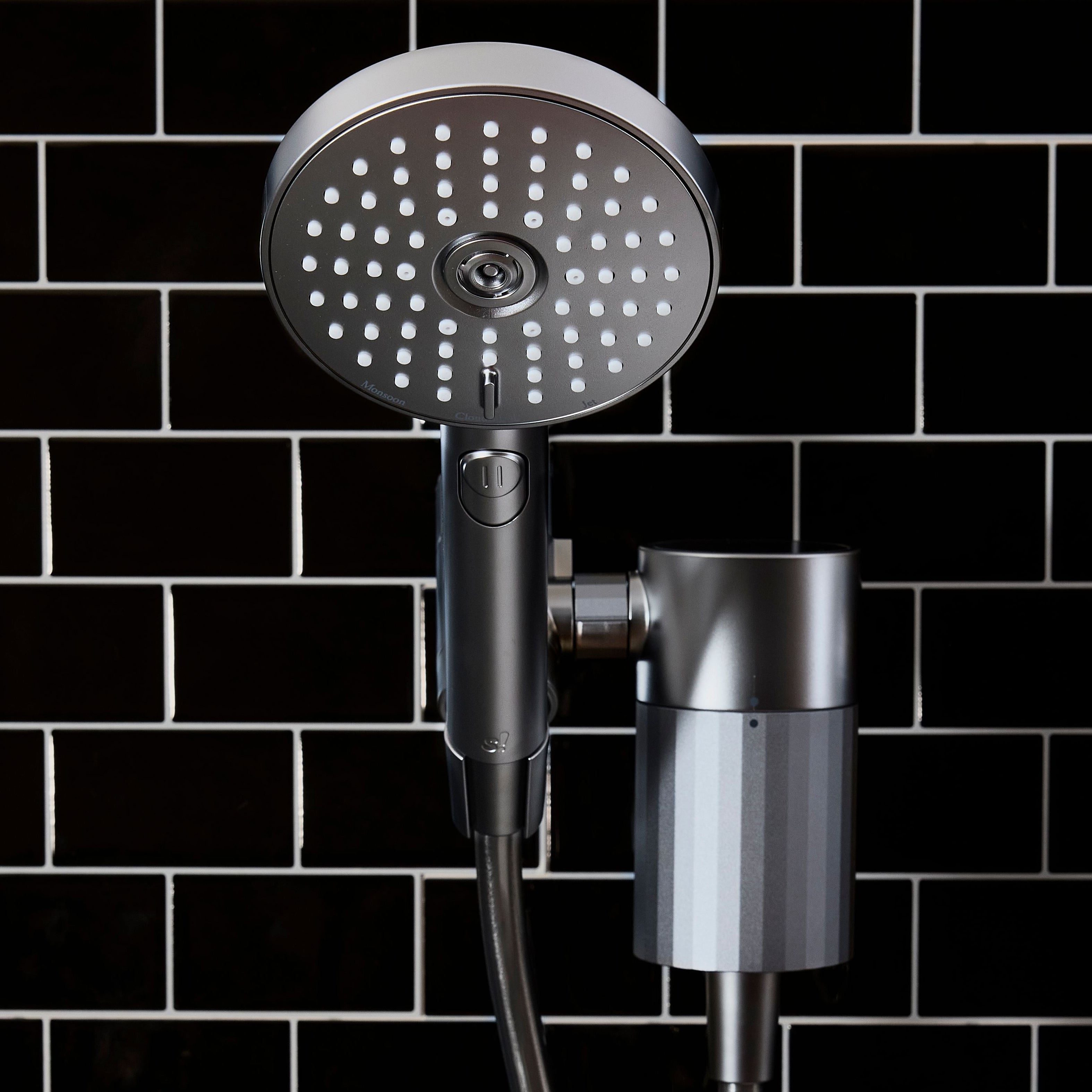 Moonlight Shower head with handheld shower attachment against a black tiled wall