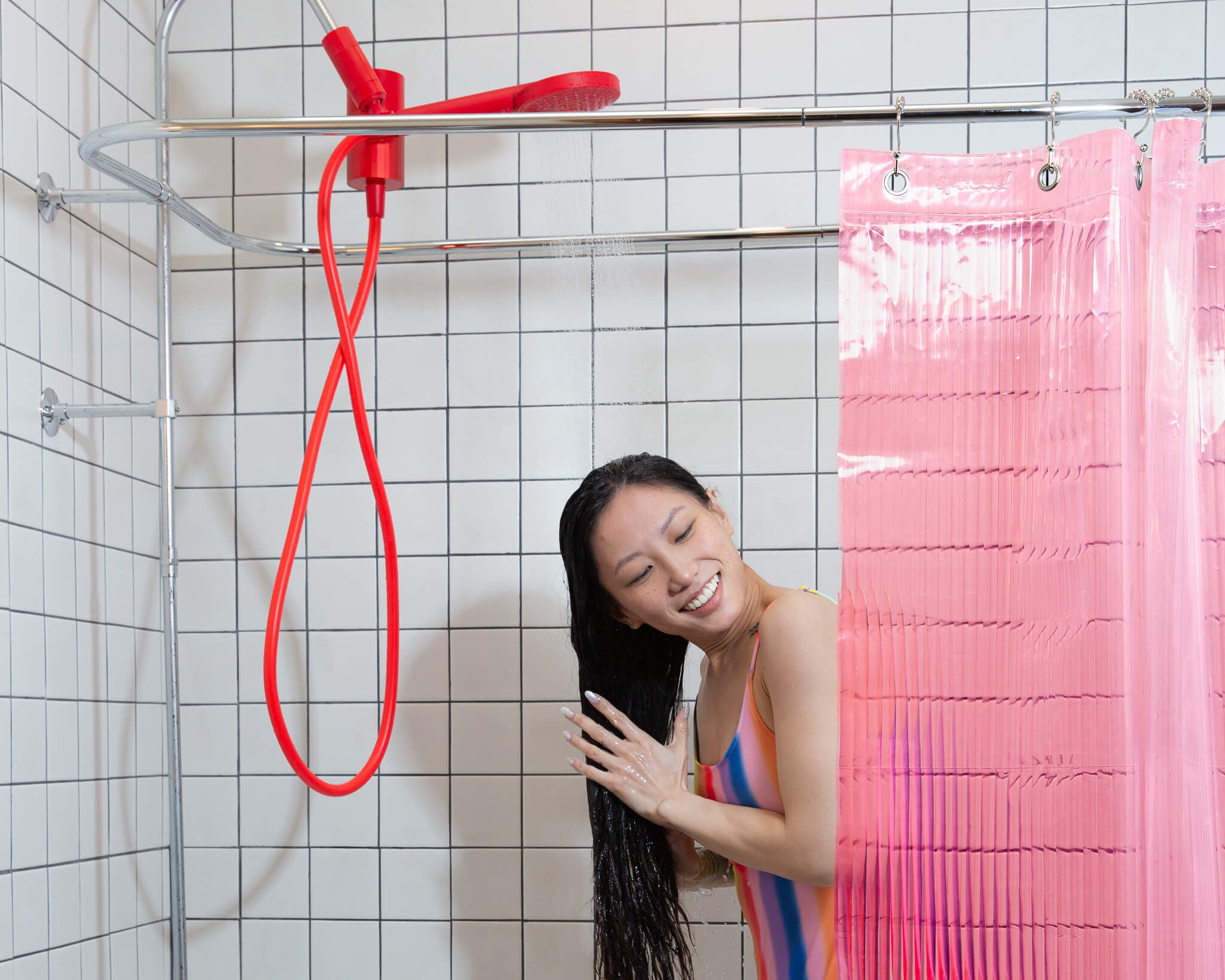 Person in bathing suit washing hair with red shower head and pink shower liner. 